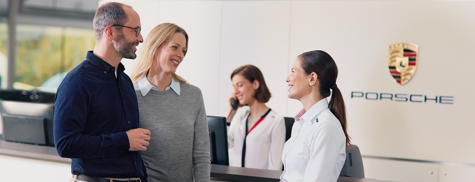 Eine Porsche Serviceberaterin berät ein Kundenpaar.