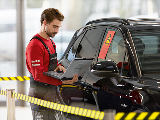 Ein Service Mitarbeiter steht als High Voltage PIWIS Tester an einem Fahrzeug.